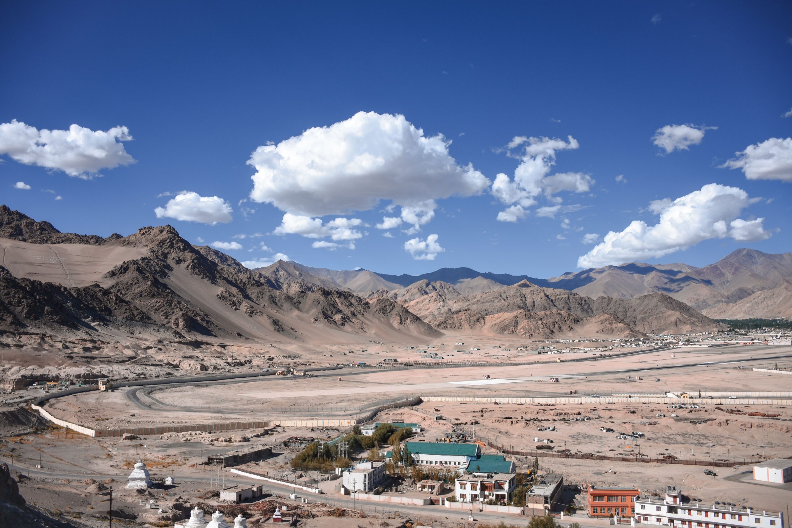 Panoramic view of Ladakh's rugged mountains under a deep blue sky with dramatic white clouds and scenic Himalayan landscape.